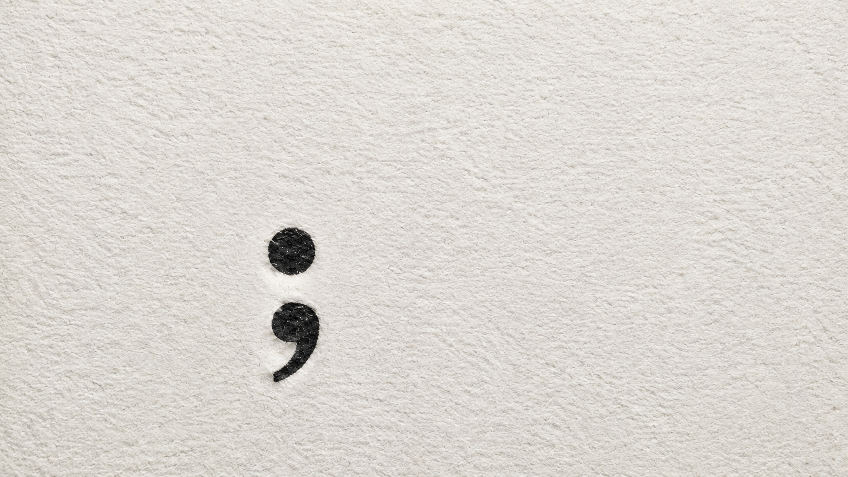 A mechanically typed semicolon on textured paperback paper